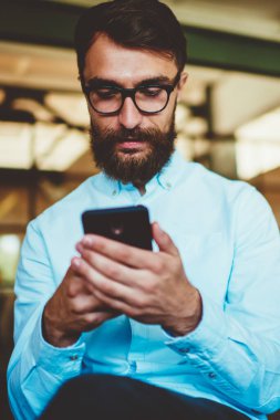 Sakallı, beyaz tenli hippi adam cep telefonuyla multimedya uygulaması üzerinden SMS mesajı gönderiyor. Gözlüklü genç erkek blogcu cep telefonuyla sosyal ağlar için yeni yayınlar yaratıyor.