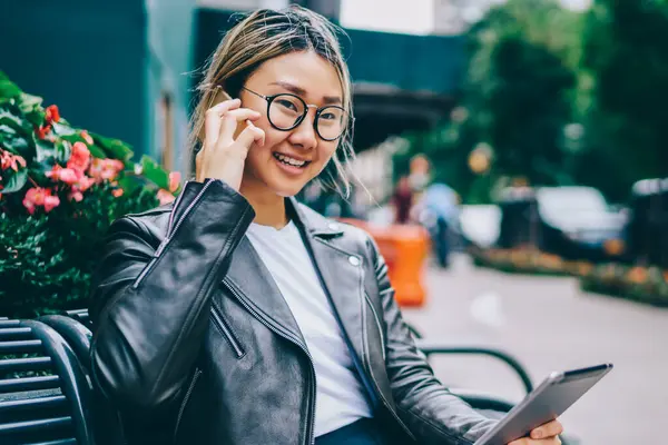 Ağ paylaşımı multimedya için mobil konuşma telefon kullanarak sahip pozitif Çinli kız açık havada, Tablet rezervasyon teyit müşteri destek operatörü ile telefonda konuşurken gülümseyen Asyalı kadın