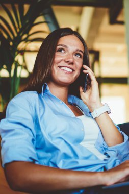 Pozitif başarılı hipster kızı cep telefonundaki bakiyeyi kontrol etmek için arıyor. Bilgisayarla kapalı alanda dinlenirken modern teknoloji ve iletişim kavramını kullanıyor.