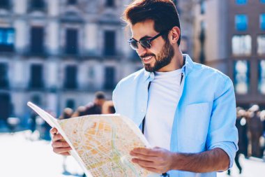 Doğru yol ve yön ayakta mimari kent merkezinde aramak için olumlu genç adam harita elinde tutan güneş gözlüğü. Mutlu erkek sevgilisi showplace yer için arayan seyahat