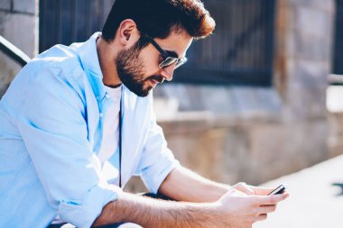 Siyah güneş gözlüklü şık genç adam, ücretsiz 4 internete bağlı modern akıllı telefondan sohbet ediyor. Gündelik kıyafet giymiş hippi adam sokakta telefonda ağlarda medyayı paylaşıyor.