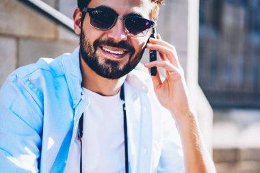 Mutlu sakallı genç adam açık havada oturma Smartphone cep telefonu ile daha fazla ve daha fazla Internet ikramiye ile yeni tarife planı için uygun koşulları ile operatör söz güneş gözlüğü görüntü kırpılmış