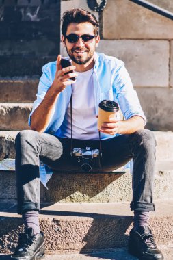 Mimari şehrin merdivenlerinde eski bir yapıyla otururken telefonla arayan neşeli sakallı adam. Kahveli olumlu blogcu cep telefonundan komik bir mesaj aldı.