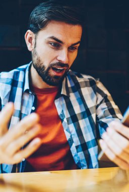 Şaşırmış gibi sakallı hippi adam akıllı 4 g internet bağlantısı üzerinden Web sitesinde online yayın izliyor. Heyecanlı erkek blogger coworking içinde oturan telefonu web sayfasında bir haberle şok