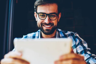 Pozitif sakallı genç adam gözlük vizyon düzeltme 4 g ile modern tablet Web sitesinde canlı akışı izlemek için internet. Touch pad aygıt üzerindeki iletim online zevk neşeli erkek blogger