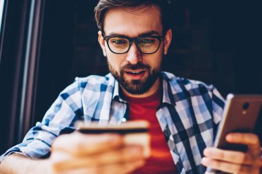 Merak optik gözlük iş smartphone aygıt üzerinde Calling kart bakarak Genç adam sakallı. Hipster adam yapma bankacılık işlem 4 g kullanarak Internet telefona bağlı.