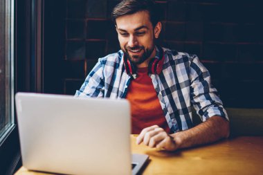 Neşeli sakallı öğrenci komik eğitsel bir Web sitesinde modern netbook aygıt izlerken boyun kulaklık ile kablosuz internet'e bağlı. Haber üstünde laptop blog okumak pozitif genç adam serbest meslek