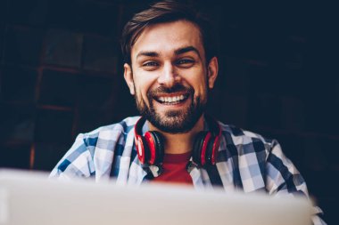 Başarılı, portre erkek freelancer uzaktan dizüstü cihaz çalışırken kameraya gülümseyen sakallı. Neşeli bu geliştirici netbook ile 4 g de alan coworking oturan kulaklıklar ile Internet