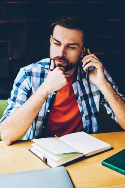 Durulması hipster adam akıllı telefon görüşmesi sırasında cep telefonu operatörü üzerinden önerisi üzerine düşünme sakallı. Tablo: Not defteri ve kitap ile öğrenim ve cep üzerinde calling düşünceli genç adam