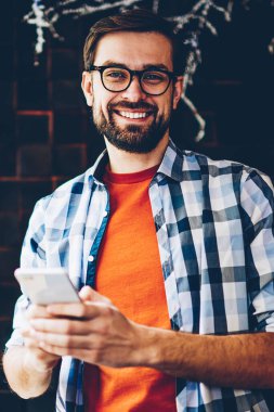 Mutlu portre alan coworking içinde smartphone aygıt ayakta kısa mesaj yazarken kameraya gülümseyen genç adam sakallı. Pozitif hipster adam Online sosyal ağlar üzerinde telefon sohbet