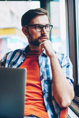 Düşünceli sakallı grafik tasarımcı düşünme üzerinde Web sitesi geliştirme ve modern dizüstü cihaz alan coworking içinde ücretsiz 4 g internet bağlantısı kullanarak, serbest çalışma pencereden dışarı seyir için fikirler