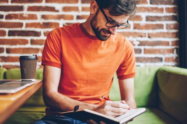 Neşeli sakallı öğrenci notlar aşağı tabii netbook aygıt ile uzay masada coworking oturan Not Defteri'nde iş yazma. Denetim listesi kayıt defterinde gözlük olumlu genç adam