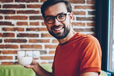 Portre kahve elinde tutan ve modern dizüstü bilgisayar yazılımı güncelleştirmek için 4 g bağlıyken kameraya gülümseyen başarılı sakallı genç adam Freelancer internet kafede oturan