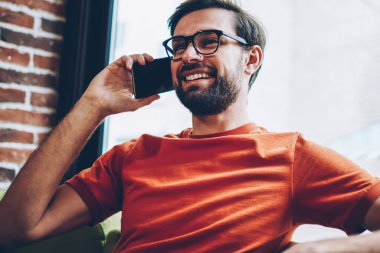 Sakallı smartphone aygıt üzerinde arama olumlu hipster adam arkadaşıyla görüşme ayarlamak için. Şık gözlük modern cep telefonu kafede oturan iç konuşurken neşeli genç adam