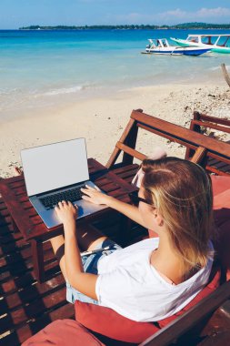 Dizüstü bilgisayarda klavye kullanan, güneşli okyanus kıyısında uzaktan çalışan yetenekli kadın milenyum klavyecisi.