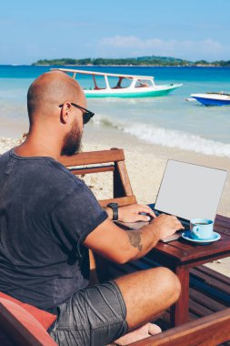 Online onun iş dizüstü bilgisayar üzerinden çalışırken okyanus kıyısında dinlenme, bin yıllık hipster adam güncelleştirme içeriği gezi hakkında yayın klavye içinde onun blogg yetenekli erkek serbest meslek