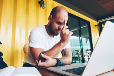 Konsantre erkek öğrenci sorun izlerken online eğitim kursları dizüstü bilgisayar, netbook, bilgi okuma projesi hakkında düşünme yetenekli erkek Tasarımcısı üzerinden sırasında çözme şaşkın