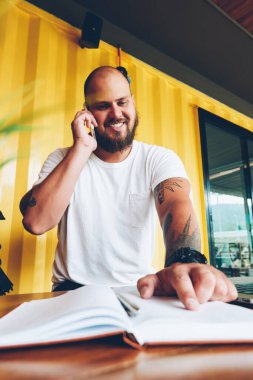 Not defteri paylaşım bilgileri cep telefonu konuşma sırasında notlarda işaret eden neşeli hipster adam. mutlu erkek öğrenci üniversite kampüsünün dizüstü bilgisayar ile oturup ödev hakkında danışmanlık arkadaş arama