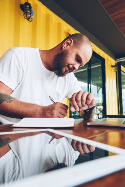 Notlar ve kol saati çalışma günü planlama ve fikirleri not defterinde yazılı zaman bakarak ciddi genç adam bu iş için dizüstü bilgisayarın yakınında oturan zamanında yönetme düşünceli erkek serbest meslek