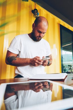 Ciddi hipster adam cep telefonu kısa mesaj, yeni uygulama ayakta masaüstü yakınındaki ofiste cihazları ile yüklemek için smartphone tutan genç bin yıllık erkek gönderme üzerinden sosyal ağlar sohbet