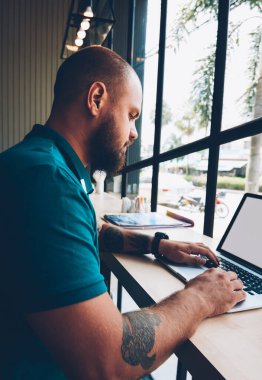 Dizüstü bilgisayar yazarak metin için blog, yetenekli erkek serbest meslek sahibi mesafe işi netbook ile sahte ekran ve kablosuz internet üzerinden yayın ile kafeteryada oturan adam Genç sakallı