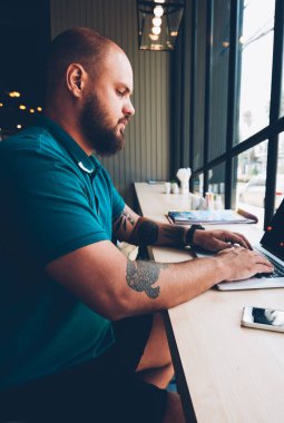 Laptop bilgisayarında dizüstü bilgisayarı olan genç adam kafeteryada uzaktan kumandalı bir iş yapıyor, yetenekli erkek netbook 'taki kafe hakkında geri bildirim yapıyor blogda serbest reklam yapıyor.