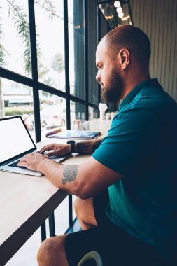 Ciddi sakallı bir erkek blogcu dizüstü bilgisayarında sosyal ağlarda ekran sohbetlerini taklit ederek mesaj yazıyor. İnternet üzerinden e-postaları kontrol eden kalem adam kafenin iç kısımlarında serbest çalışmalar yapıyor.