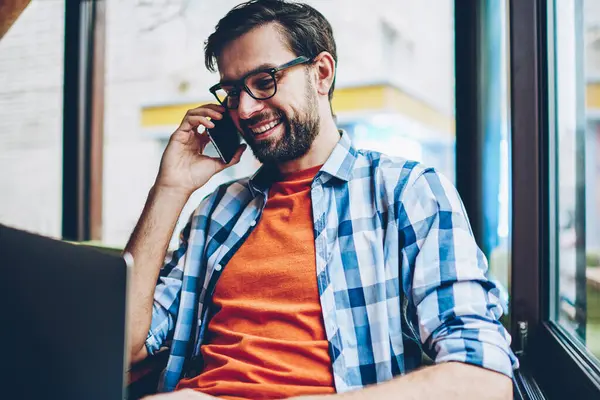 Happy sakallı genç adam gözlük smartphone yazılım yolu ile radyo 4 g modern dizüstü bilgisayarda güncelleştirilirken iletişim internet. Netbook hücresel oturma konuşurken olumlu hipster adam