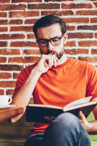 Akıllı hipster öğrenci ders kitabı hazırlama semineri için bilgilerin öğrenme konsantre. Coworking modern netbook ile masada oturan görev çalışmaya düşünme dalgın genç adam