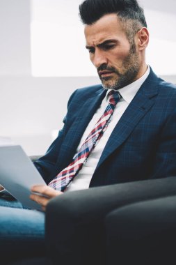Konsantre deneyimli olgun gurur CEO'su muhasebe raporları, office koltukta oturan kağıtlara okuma formal giyim giymiş. Dalgın işadamı 50 yaşında mali bilgilerini kontrol