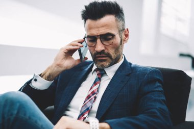 Zaman denetleme ve toplantı üzerinde bekleyen bir seyretmek ararken meşgul emin işadamı orta yaşlı istek-e doğru Smartphone cep telefonu ile ortak. Formal giyim üzerinde modern cep konuşurken gurur CEO'su deneyimli