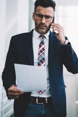 Başarılı bir iş adamı 50 yaşında metin belgeleri smartphone aygıt üzerinde konuşurken elinde olan portresi. Kendine güvenen gurur CEO'su resmi aşınmaya kameraya bakarken modern telefonla arama
