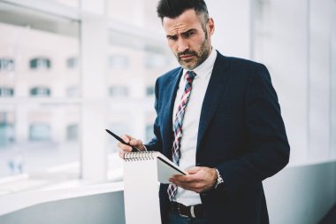 Not Defteri'nde yaparken kameraya bakarak formal giyim giyinmiş emin gurur CEO'su 50 yaşında portresi. Kayıt defter daimi ofis yazma başarılı olgun iş adamı