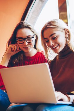 Pozitif kız öğrenci eğitim webinar birlikte kablosuz bağlantı ve dizüstü bilgisayar kullanarak coworking uzayda genç kız arkadaşlar eğlenmeye izlerken zevk netbook üzerinde boş zaman üzerinde ağ