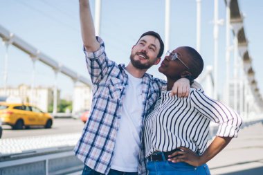 Gülümseyen neşeli sakallı adam günlük giysiler içinde selfie çekiyor cep telefonu kullanıyor gözlüklü Afro-Amerikan kadını kucaklıyor kısa saçlı sokaklarda dolaşıyor.