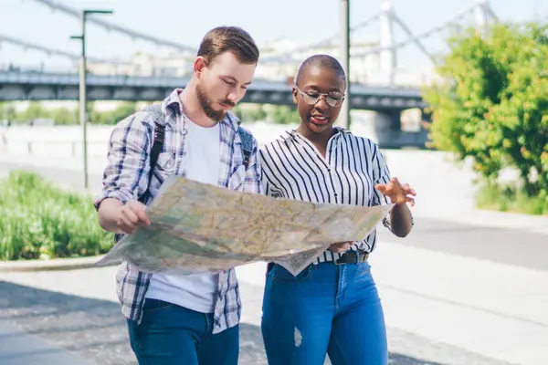 Konsantre olmuş, genç, çeşitli turistler günlük giysiler içinde ellerinde harita tutuyorlar ve caddeleri gezerken kendilerine yer arıyorlar.