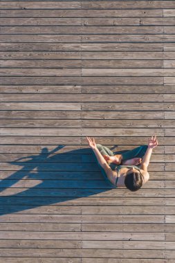 Yoga elbiseli kadın, meditasyon yapıyor ve lotus poz veriyor. Tahta zeminde oturuyor. Sol taraftan gölgesi düşüyor.