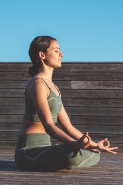 Nilüfer çiçeği pozisyonunda sakin bir kadın, dizlerinin üzerinde elleri ve gün doğumunda ahşap patikada gözleri kapalı.