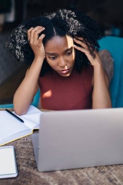 Siyah, kıvırcık saçlı, sıradan giyinmiş, dizüstü bilgisayar kullanan, kafeteryada ellere dayanma projesine bakan bir kadın.