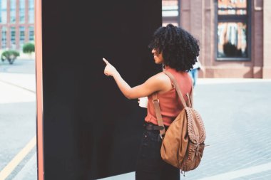 Siyah, parlak, Afro saçlı, günlük giysili ve sokakta yürüyen reklam panolarını gösteren çantalı bir gezginin arka planı.