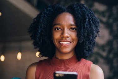 Afrika kökenli, parlak, kıvırcık saçlı, rahat giyinen, akıllı telefon kullanan, sosyal medyada vakit geçiren, modern kafe kızı.