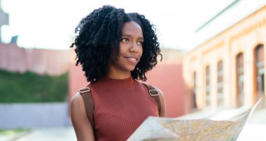 İyimser kıvırcık saçlı, günlük kıyafetlerle gülümseyen siyah turist haritayı kullanarak şehri geziyor güneşli bir günde gözlerini kaçırıyor.