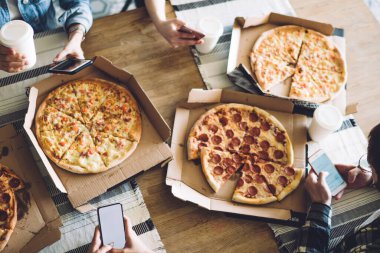 Yukarıdan gelen leziz, iştah açıcı pizza paketleri masada oturan ve cep telefonlarını karıştıran mahsul aç arkadaşlar için.