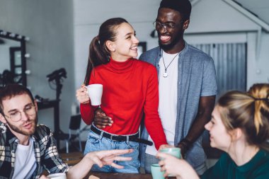 Çok ırklı genç hippiler lezzetli pizzalarla yuvarlak masa çiziyor sıcak içeceklerin tadını çıkarıyor ve şık bir evde birlikte eğleniyorlar.