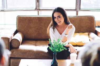 Şık giysili bir bayan kanepede oturup el ele tutuşup konuşuyor ve genç bir adam ve bir kadın önünde oturuyor.