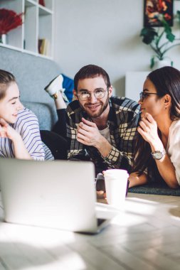 Erkek ve bayan arkadaşlar hafta sonunu sohbet ederek ve dizüstü bilgisayar izleyerek rahat bir oturma odasında yan yana yatarak geçiriyorlar.