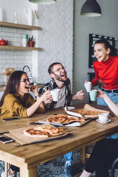 Neşeli, çoklu etnik gruplardan oluşan bir grup günlük giysiler içinde doğum günü kutlamaları ve evde pizza eşliğinde masaya gülüp kadeh kaldırıyorlar.