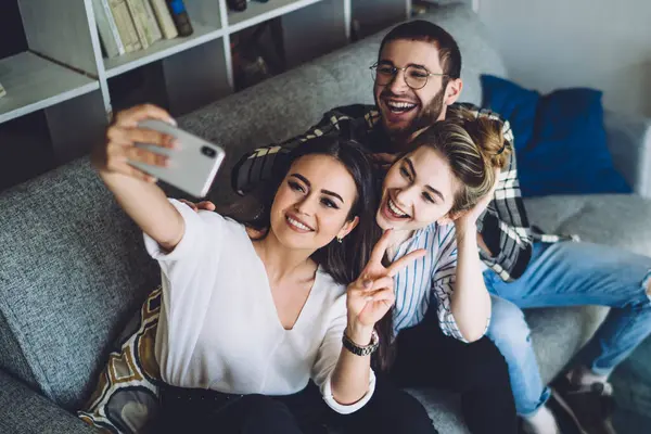 Yukardan genç, mutlu, şık moda öğrencileri rahat modern tasarım oturma odasında rahat koltukta oturup selfie çekiyorlar.