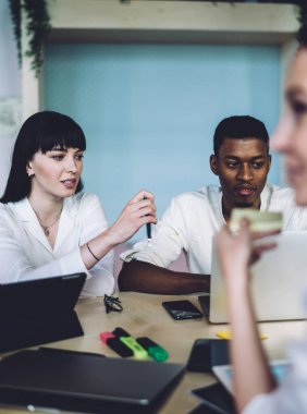 Ciddi niyetle çok ırklı ofis çalışanları resmi giysiler içinde büroda kağıtlarla otururken sohbet ediyorlar.