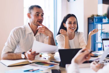 Resmî giysiler içinde hevesli iş adamları modern ofiste grafik ve belgelerle masa başında otururken sohbet ediyor ve dizüstü bilgisayarda geziniyorlar.